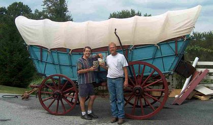 Shawn House & Jim stand in front of an Original Conestoga Wagon covered in hemp canvas.