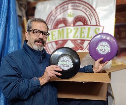 standing holding purple and black frisbee with hempzels logo with hempzels banner in background
