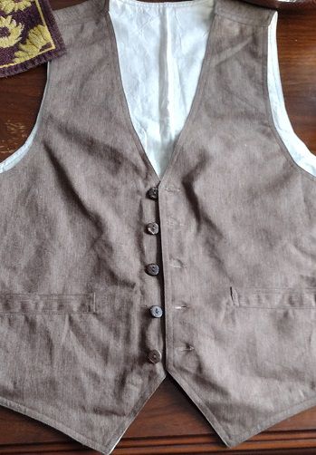 Brown fabric white backing vest with 5 buttons on brown table. Hempvest.