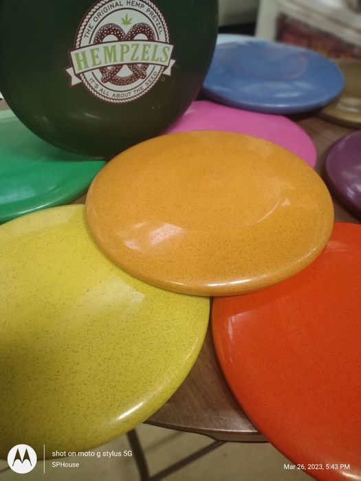 Photographic image of circular frisbees in orange, yellow, green, pink, red, black, purple laying on each other.