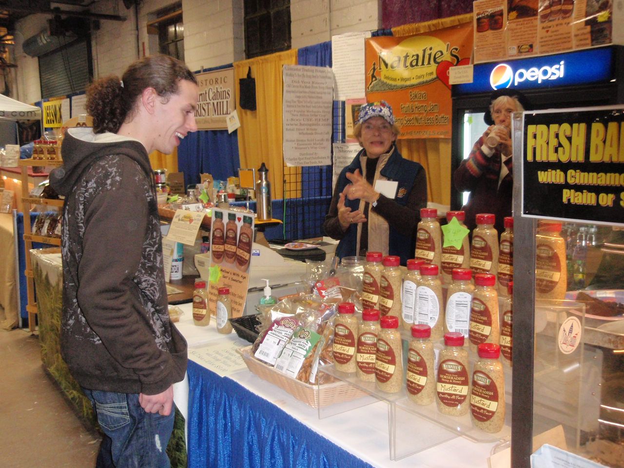 Young bearded customer stands in front of PA Farm Show booth with mustard and Shawns parents helping him.