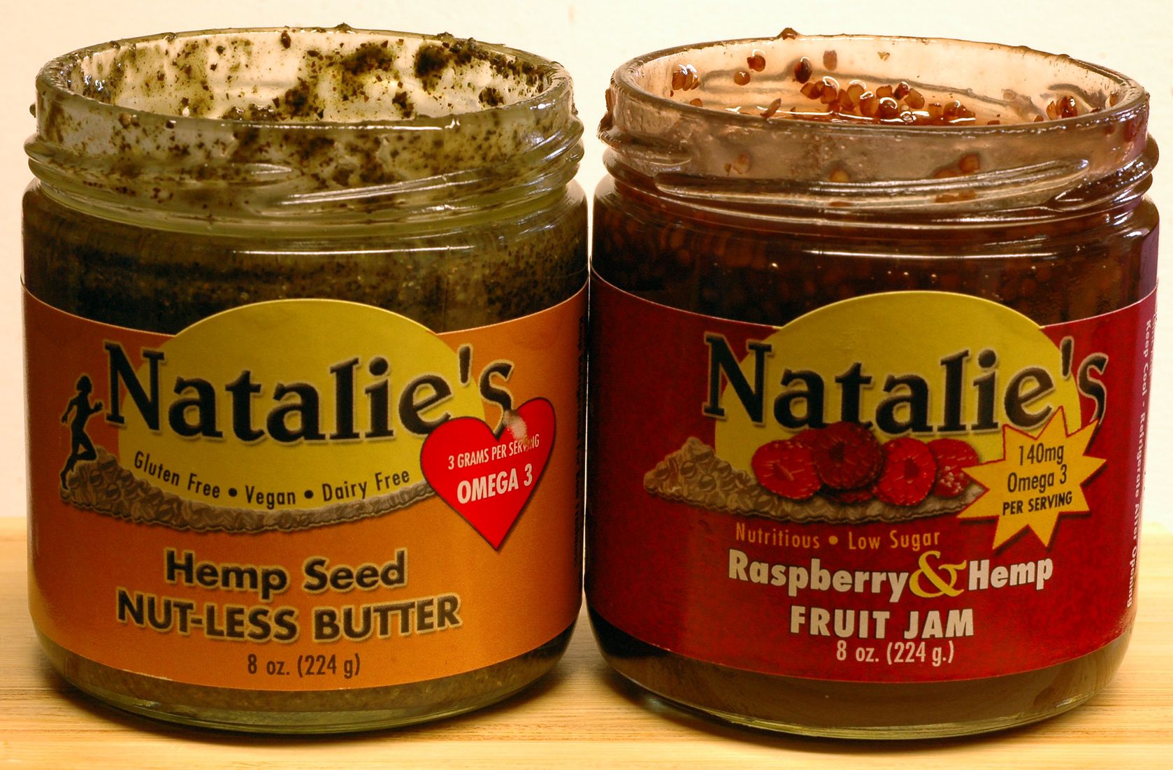 Two jars with lids off, left is light brown label with dark hemp seed on the right is red labeled raspberry filled jam jar.