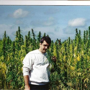 Shawn standing in cannabis field holding a hemp flowering with hemp grain in the daylight