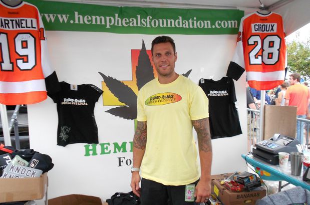 Riles Cote in yellow t-shirt in his booth with Philadelphia Flyer and Hemp heals colors orange green.