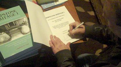 Author Les Stark signing his book Hempstone Heritage with books stacked beside him.