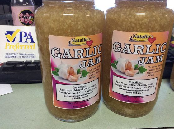 Two large glass jars of yellow garlic jam with pink labels both jars sitting on a desk.
