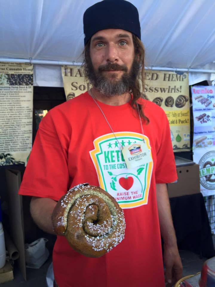 Ambassador Lazlo holds up hot soft pretzel swirl in his red t-shirt in front of the Hempzels booth.