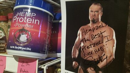 Blue & red container of hemp protein and wrestler without his shirt on flexing his muscles.
