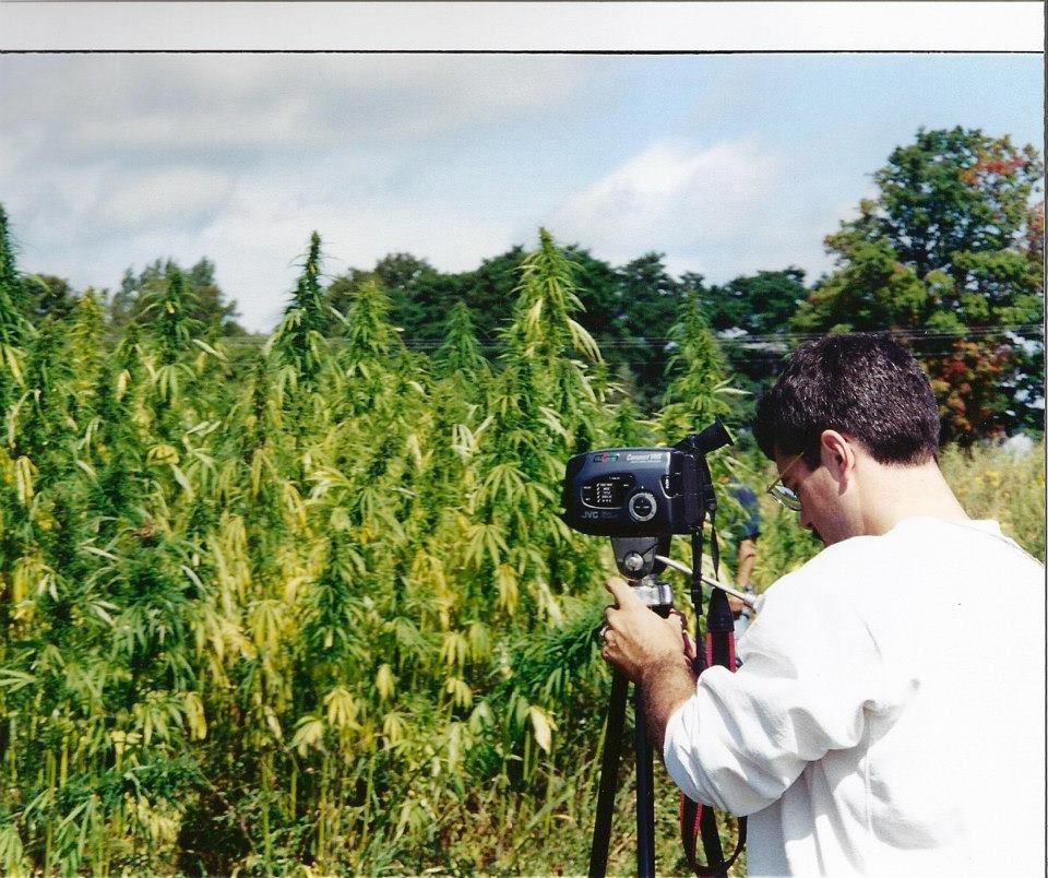 Shawn in Hemp white hemp sweatshirt setting up VCR camera to video tape hempfields in Canadian field.