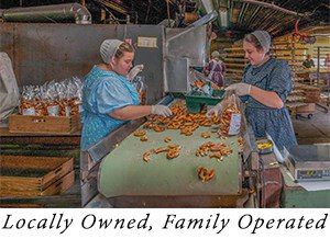 Two bonneted ladies in blue dresses with gloves on hand pack hemp pretzels coming out of a bakery shoot.